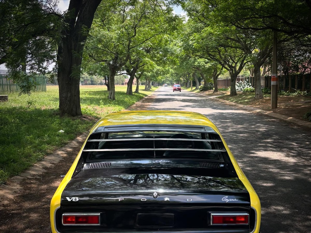 Inbound RHD yellow classic car on a tree-lined road